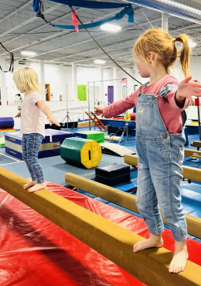 Two toddlers walk side-by-side practice beams with their arms out