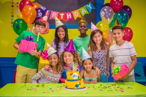 A birthday crew in party hats gathers around the cake at the decorated party table